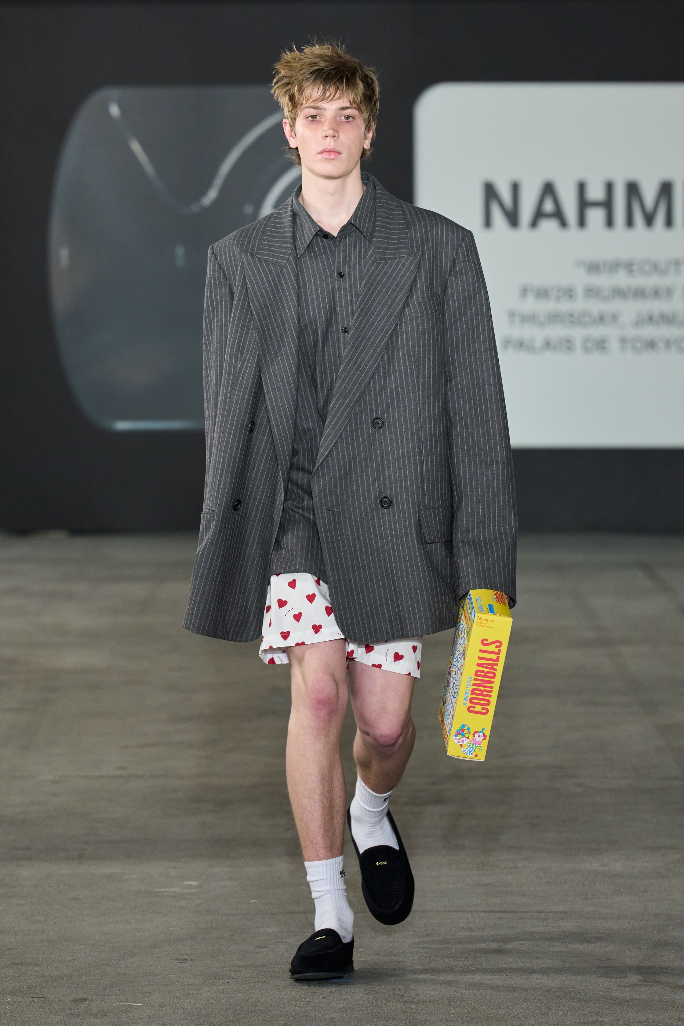 Nahmias 2026秋冬将洛杉矶滑板文化与怀旧流行符号并置，打造一场带有讽刺意味的青春景观。宽松裤装、学院感上衣与玩味图案形成轻松而不设防的氛围，滑板与面具式造型强化表演性。系列并不追求精致，而是通过“不完美”的搭配捕捉西海岸随性、反精英的生活态度，呈现一种带着玩笑感的现实主义-顽石频道趋势研究